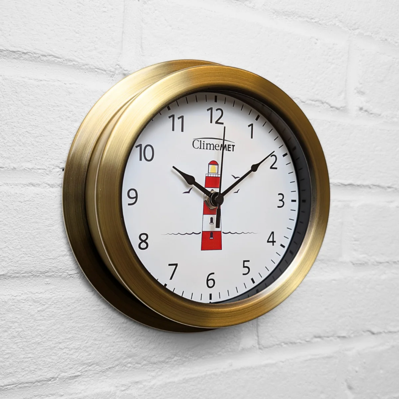 Wall clock with brass frame and lighthouse design on a white background